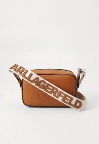 Brūna ādas plecu soma ar perforētu logotipu, sudraba detaļām un krēmkrāsas siksnu ar uzrakstu „Lagerfeld” biezos burtiem.