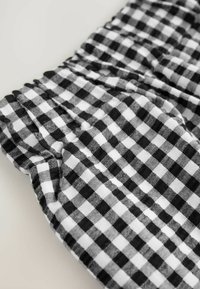 Tissu vichy noir et blanc avec une texture plissée, présentant de petits motifs à carreaux. Matériau doux et léger avec un léger aspect brillant.