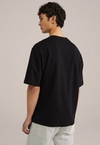 Černé bavlněné tričko s krátkým rukávem a volným střihem. Design obsahuje kulatý výstřih a hladkou strukturu.