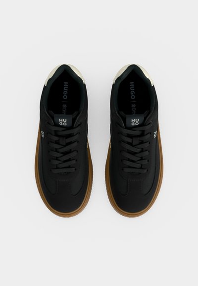 Paire de baskets basses noires avec semelles marron, lacets noirs et accents blancs au talon, brandées "HUGO" sur la languette et les côtés.