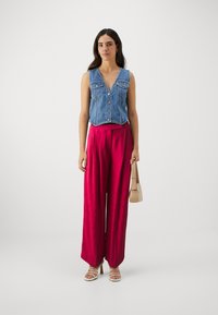 Denim vest, mille esipaneel ja roosa laiad püksid, millel on peen muster, ning beež käekott. Mudel kannab rihmadega sandaale.
