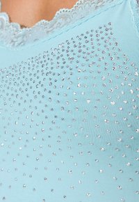En ljusblå ärmlös topp med spetsdetaljer, prydd med silverfärgade gnistrande stenar som är arrangerade i ett spritt mönster över tyget.