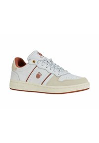 Zapatilla deportiva blanca con acentos de ante beige, rayas rojas horizontales y ojetes dorados. Presenta una suela de goma texturizada y una puntera perforada.