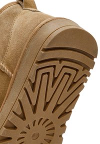 Sandfarbene Wildlederstiefelsohle mit einem strukturierten Gummiprofil, das kantige Muster und ein zentrales kreisförmiges Design für besseren Grip aufweist.