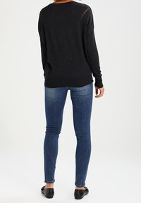 Suéter negro de manga larga con un corte relajado, combinado con jeans de mezclilla azul ajustados. La textura parece suave, y los jeans tienen un ligero desgaste.