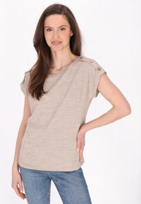 Beige, kortærmet top med afslappet pasform, med knapdetaljer på skuldrene, lavet af blødt, tekstureret stof. Bæres med blå jeans.