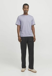 Camiseta de algodón lila con mangas cortas, combinada con pantalones negros. Cuenta con un escote redondo y un corte relajado. Los zapatos son beige con detalles.