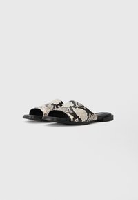 Flache Slide-Sandalen mit einem strukturierten Schwarz-Weiß-Schlangenhautmuster, offener Zehenpartie und einer glatten schwarzen Sohle.