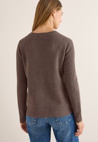 Brauner gerippter Strickpullover mit langen Ärmeln, Rundhalsausschnitt und lässiger Passform, kombiniert mit blauen Jeans. Weiche Textur und dezenter Fall.