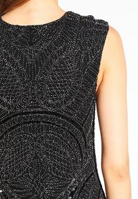 Ärmlös svart klänning med intrikata mönster av silverpärlor och paljetter på baksidan, bärs av en person med ljus hy.