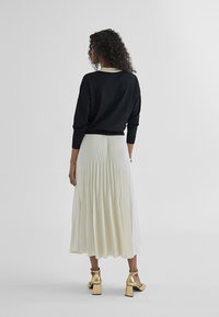 Black sweater with long sleeves paired with a white pleated skirt and gold block-heeled shoes, showcased from the back.