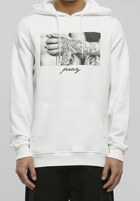 Sudadera blanca con capucha y un gráfico frontal de una mano tatuada sosteniendo joyas. Cuenta con un bolsillo tipo canguro y capucha con cordón. Textura de tela suave.
