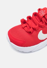 Piros sportcipő texturált felsőrésszel, amelyen kifejezett bordázás található és egy fehér Nike logó díszíti. A fűzők integráltak és figyelemfelkeltően lettek megtervezve.