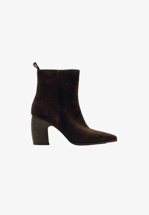 Stivaletto in suede marrone con punta affusolata, tacco spesso e scanalato, e un'asola sul retro per indossarlo facilmente. Texture liscia e design elegante.