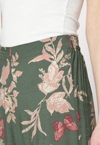 Kalhoty s květinovým vzorem, zelená látka s růžovými a červenými květinami a motýly. Elastický pas, lehký, splývavý design.