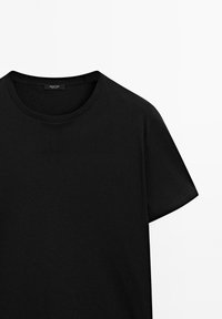 T-shirt noir à manches courtes et col rond avec une petite étiquette de marque à l'intérieur, au niveau de l'encolure arrière, sur fond blanc.