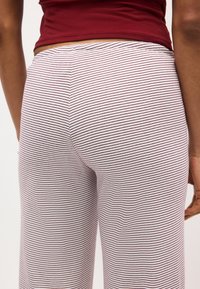 Άτομο που φοράει άσπρο παντελόνι με λεπτές κόκκινες οριζόντιες ρίγες και σκούρο κόκκινο πάνω μέρος, εμφανιζόμενο από τη μέση και κάτω, από πίσω.