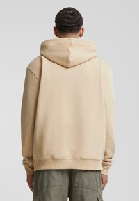 Felpa beige realizzata in morbido tessuto, dotata di cappuccio con coulisse, polsini a coste e una vestibilità leggermente oversize. Design semplice e pulito.