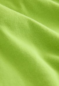 Tissu vert citron doux avec une texture fine de tricot visible et des plis délicats créant des ombres douces.