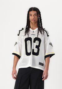 White mesh jersey with black accents and number 03. Features short sleeves, rounded neckline, and logo on the chest and sleeve. Black cargo pants.
