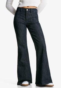 Jeans negri din denim evazați cu talie înaltă, buzunare frontale și un finisaj elegant. Materialul texturat completează designul modern și forma cu picior larg.