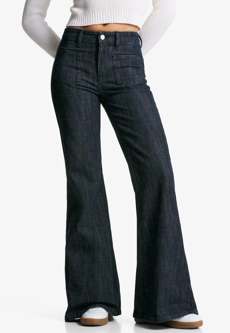 Jeans negri din denim evazați cu talie înaltă, buzunare frontale și un finisaj elegant. Materialul texturat completează designul modern și forma cu picior larg.