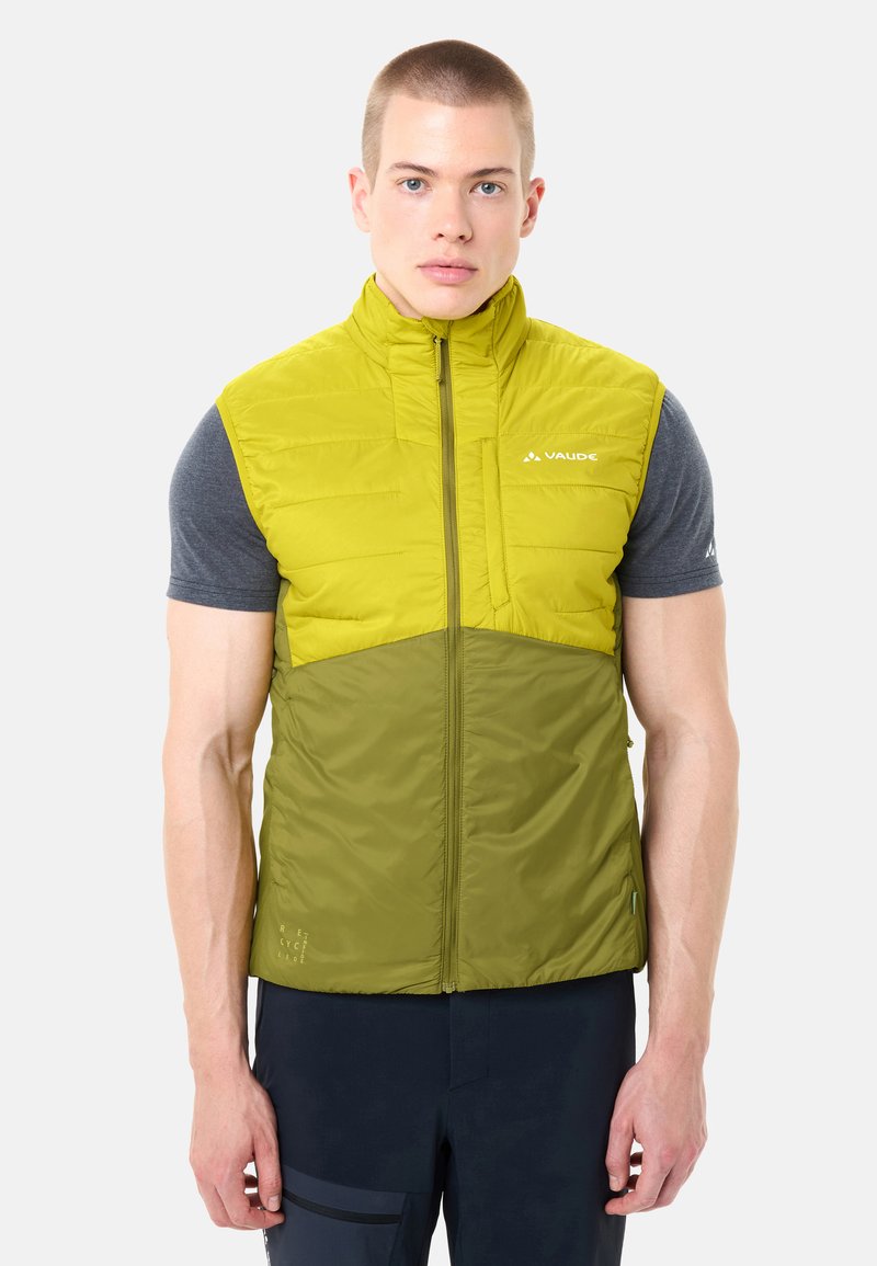 Mann trägt eine zweifarbige grüne, ärmellose gesteppte Weste über einem dunkelgrauen Kurzarmshirt und steht vor einem einfarbigen Hintergrund.