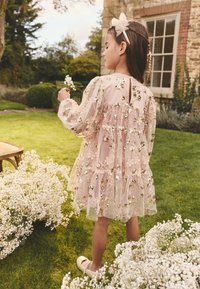 Hämaralt roosa kleit kihiliste volangide, lillbroderii ja litritega. Stiilitud sobiva peapaela ja valgete lilledega ümbritsetuna.