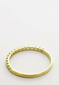 Guldfärgad metallarmband med en slät yta, som har jämnt fördelade cirkulära urklipp längs den yttre kanten.