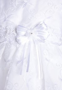 Valkoinen mekko, jossa on kukka-ompelua ja koristeellinen satiini-nauhoista tehty bow. Bow'ssa on kangaskukka ja keskellä helmi.