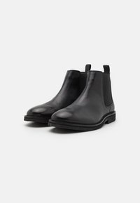 Botas Chelsea de piel negra con paneles laterales elásticos, punta redondeada y suela de goma. Textura suave con acentos mínimos. Adecuadas para un uso casual.