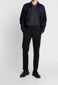 Czarna dżinsowa kurtka noszona na szarym swetrze w serek, zestawiona z czarnymi spodniami i czarnymi sznurowanymi butami. Minimalistyczny design, dopasowany krój.