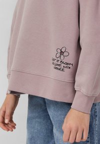 Jasnoróżowa bluza z kwiatowym wzorem i haftowanym tekstem "NIECH ROZKWITA W MIŁOŚCI Z NATURĄ." Z ribbowanymi mankietami i dołem, o miękkiej fakturze.