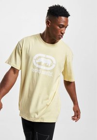 Gul bomulds t-shirt med korte ærmer, prydet med et hvidt grafisk logo og tekst foran, afslappet pasform og let vævning.