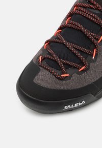 Musta ja harmaa kiipeilykengät, joissa on teksturoitu pinta, oranssit nauhat ja kumipohja; sivussa on logo.