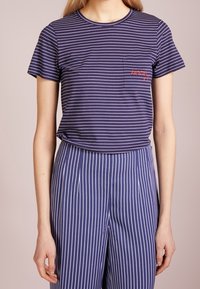 Námořnické modré pruhované tričko s krátkými rukávy a kulatým výstřihem, s malým červeným vyšitým detailem na kapsičce na prsou.