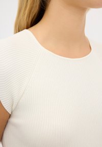 Ribbed, světle krémový top s kulatým výstřihem a krátkými rukávy. Má strukturovanou tkaninu a přiléhavý střih, který zvýrazňuje jemné švy.