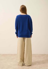 Blå stickad tröja med vida ärmar, kombinerad med beigefärgade randiga vida byxor. Mjuk textur med en avslappnad silhuett.