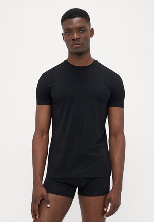 Schwarzes kurzärmeliges T-Shirt aus glattem Baumwollstoff, mit rundem Hals und taillierter Form, kombiniert mit schwarzen eng anliegenden Shorts.