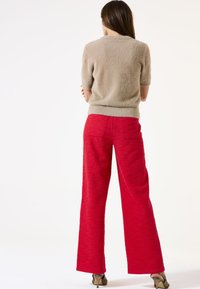 Pull beige à manches courtes et pelucheux associé à un pantalon large texturé rouge taille haute. Sandales à talons visibles.