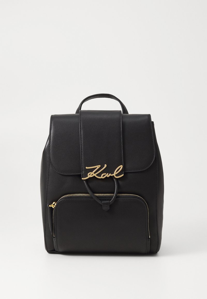 Black leather backpack with a gold signature accent, a flap top closure, and a front zipper pocket. Smooth texture with structured shape.