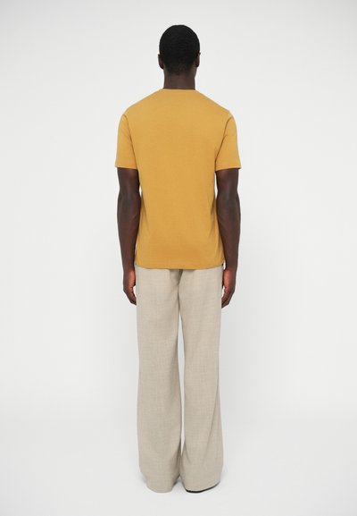 Horčicovo žlté tričko s krátkym rukávom v kombinácii s ľahkými béžovými nohavicami s širokými nohavicami, s jemnou textúrou a jednoduchým dizajnom, zobrazené zozadu.