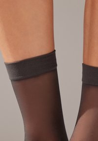 Transparent svarta strumpor som går upp till låren, med ett mjukt, strukturerat mörkt band upptill och en slät, genomskinlig bendel.