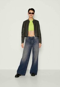 Jaqueta cropped de couro preto, top cropped verde néon e jeans largos desbotados azuis com um detalhe em corrente prateada. Usado com sapatos pretos.