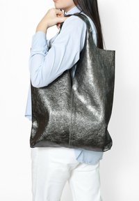 Metalen grijze tote bag heeft een gladde, glanzende textuur en versterkte schouderbanden. Ontworpen voor functionaliteit met een ruime binnenkant.