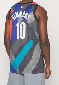 Basketbalový dres, šedý s abstraktními vícemořádovými vzory. Na zadní straně velký nápis "SIMMONS" a číslo "10". Vyrobeno z prodyšné síťoviny.
