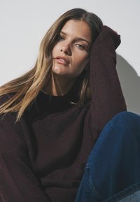 Bordó pletený svetr s kulatým výstřihem a dlouhými rukávy, kombinovaný s modrými džínami, které mají pohodlný střih a měkkou texturu.