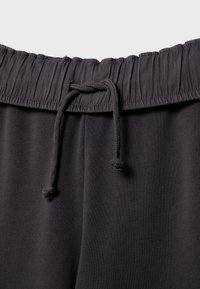 Ceinture élastique noire avec cordon noué sur un pantalon en tissu doux, vue en gros plan sur un fond clair.