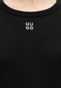 Encolure de chemise noire avec petit logo blanc "HUGO" brodé au centre devant, sous le col.