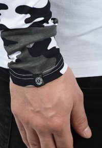 Langarmshirt met een wit en zwart camouflagepatroon. Voorzien van een contrasterende zwarte manchette met een ronde logotag. Zachte katoen stof.